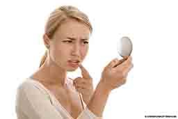 A woman uses a hand mirror to inspect a cold sore. 