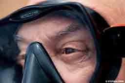 A close-up image of an older diver wearing a mask. The image shows just his eyes.