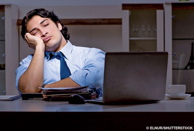 A man in shirt and tie falls asleep at his desk in front of his laptop.
