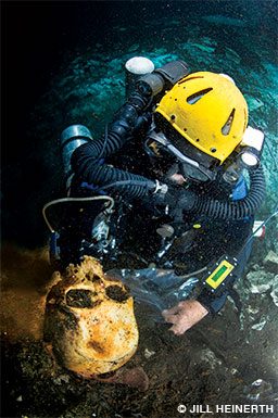 Kakuk in his dive gear lifts an ancient skull to examine it.
