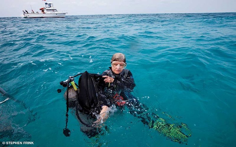 An older female diver collects her gear while wading in the water.