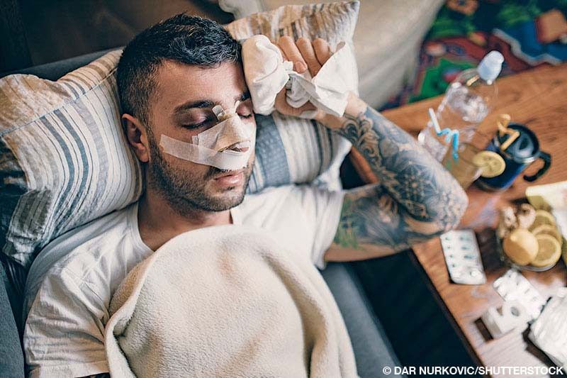 A man with a bandaged nose rests with his eyes closed after rhinoplasty surgery.