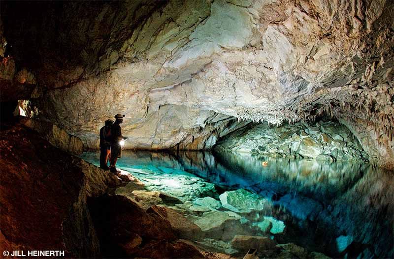 Researchers use a flashlight to view an underground cave filled with water.