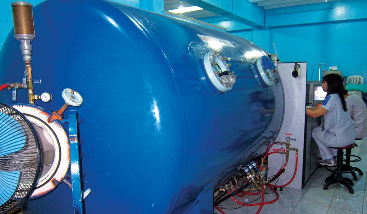 A blue hyperbaric chamber is being monitored by a nurse in blue scrubs