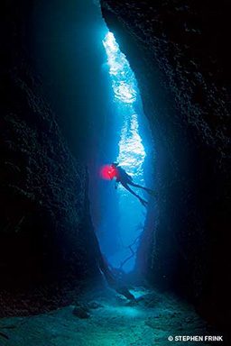 A diver enters Leru Cut, one of the Solmon Islands' most iconic dive sites. There is a red light from the diver's torch