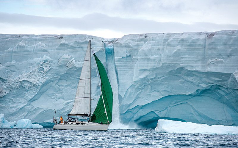 Boat with green sails floats near ice caps