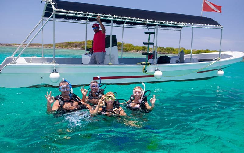 Four divers in dive gear float next to a dive boat