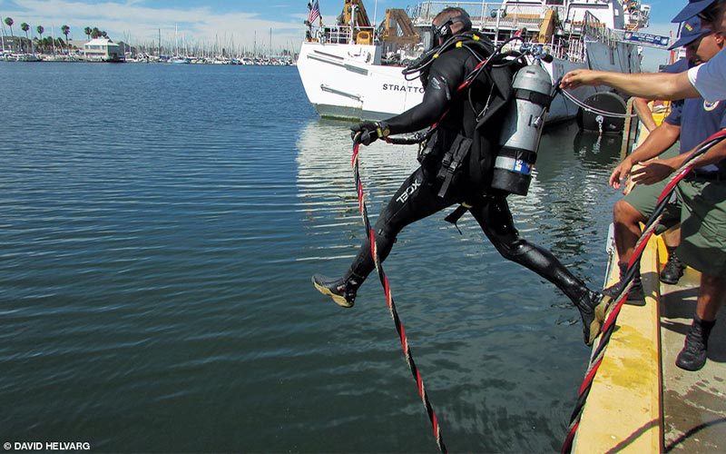 A U.S. Coast Guard Diver jumps off a dock and into the water