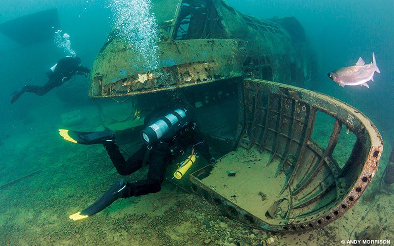 Two divers approach a shipwreck in a fresh-water environment