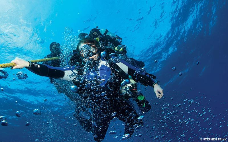 Divers hold onto a line and make a safety stop