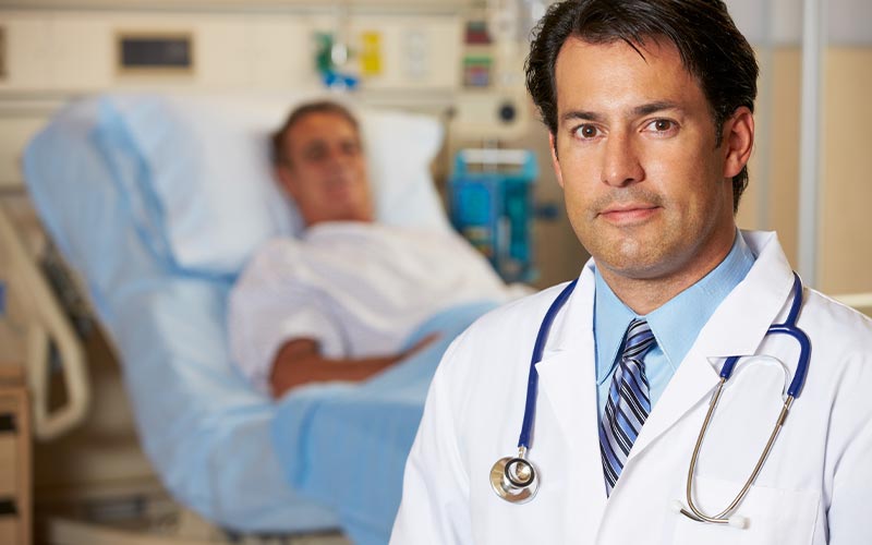 Doctor stands in the foreground to a patient lying in a hospital bed