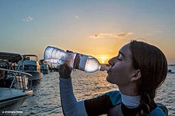 Female person drinks from a water bottle at sunset