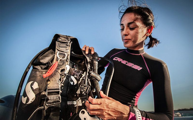 A woman with pink-and-black wetsuit gets her scuba gear ready before diving