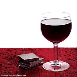 Glass of wine on right and pile of chocolate pieces on left. All on red tablecloth
