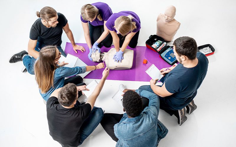 Group of people gather around a purple yoga mat to learn CPR techniques