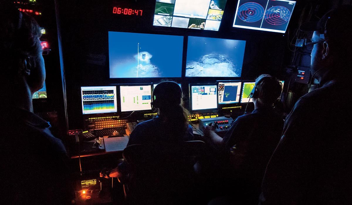 Group of researchers stand around computer monitors in dark room