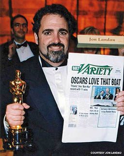 Jon Landau holds up a newspaper headline and his Oscar trophy