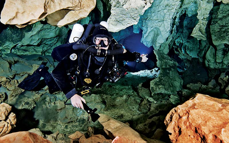 Man, holding a flashlight and wearing a drysuit, dives into a cave