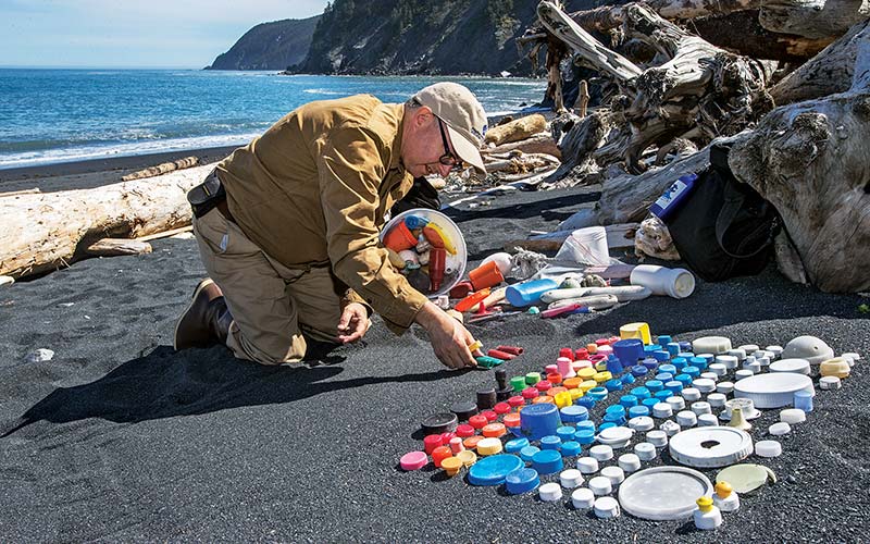 Man kneels on beach and organizes plastic trash by color