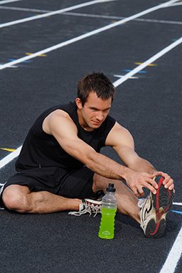 Man stretches on a track next to a green sports drink
