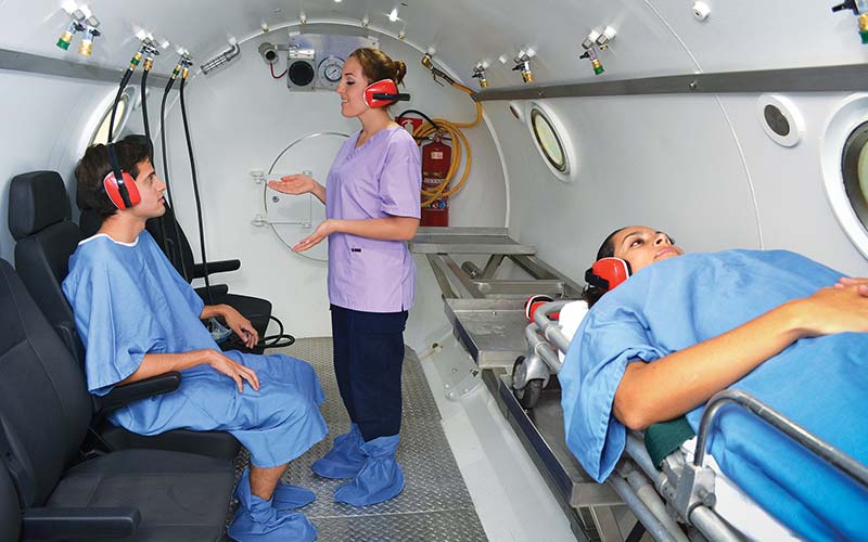 Nurse works with two people inside hyperbaric chamber