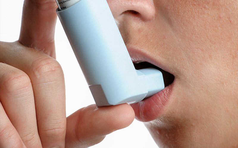 A person places their asthma inhaler right on their lips and is ready to take a puff