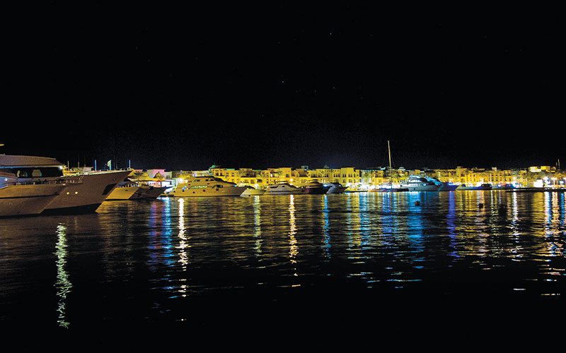 Port Ghalib Marina at night and the boats and buildings are lit brightly 