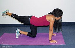 A personal trainer is in table-top position and crossing her extended right leg over her bent left leg