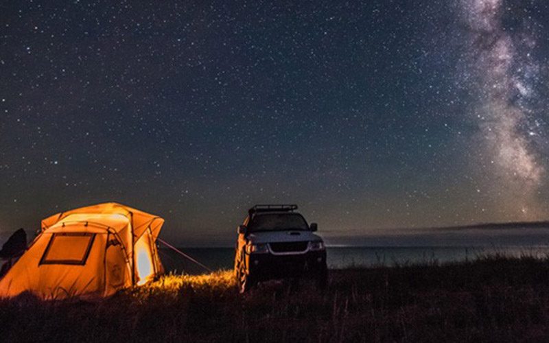 At night time, a Jeep is posed next to a lit-up tent