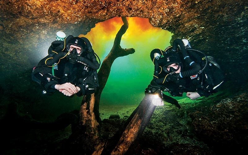 Two cave divers float through a hole
