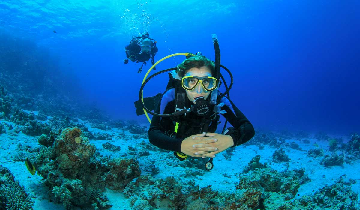 A female diver is in the foreground with her hands clasped. A male diver is in the background.