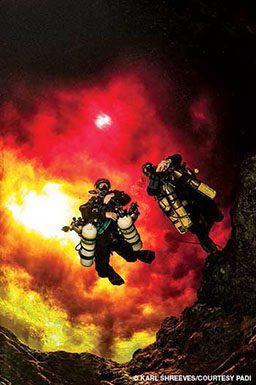 Two divers swimming away from what appears a giant fire