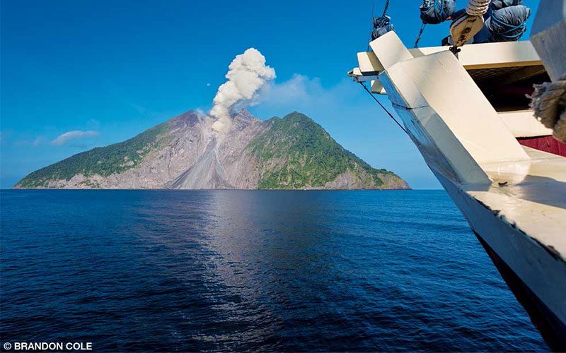 A volcano blows smoke into the air. The volcano is part of an island in the ocean