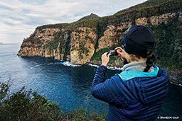 A lady takes a photo of cliffs in Tasmania