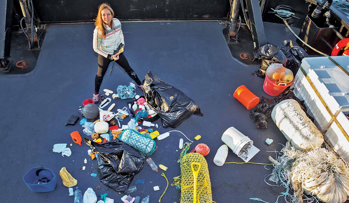 Woman stands next to giant pile of trash