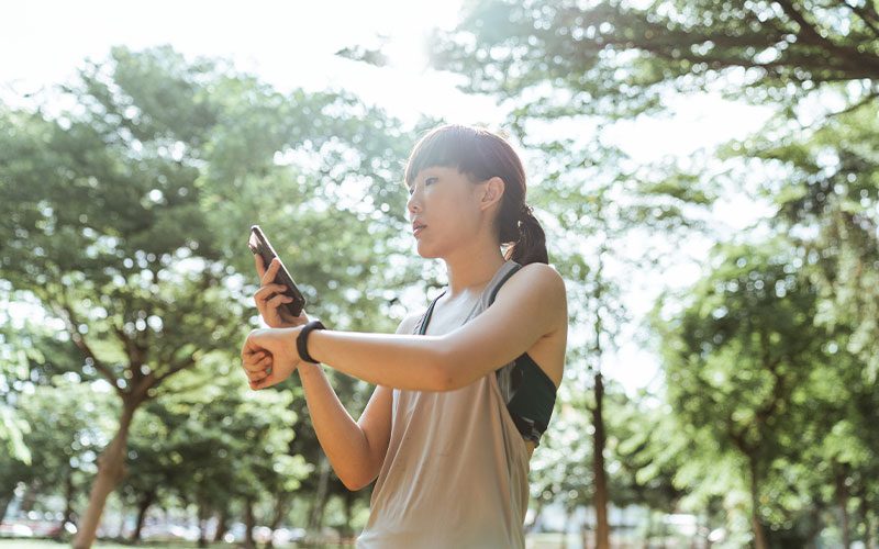 A woman tracks her smart watch that is worn on her left wrist. Her smart phone is in her right hand.