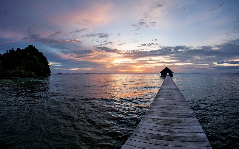 A dock, with house at the end, rests at sunset