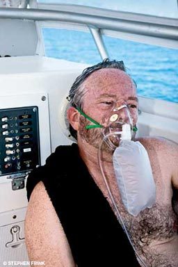 A man sits on a boat wearing an oxygen mask