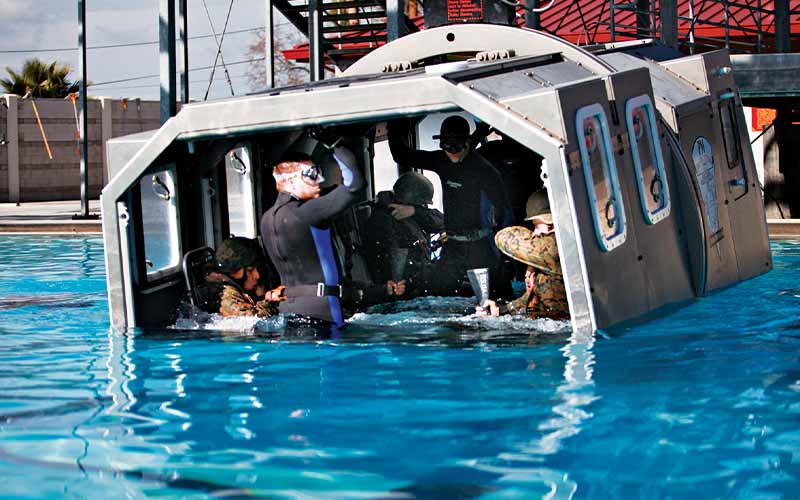 A metal hull full of divers is lowered into a pool