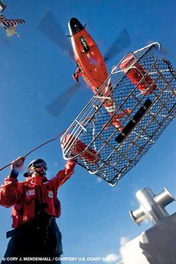 A person helps load a wire care below a flying orange helicopter