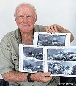 An old bald man holds several black-and-white photos