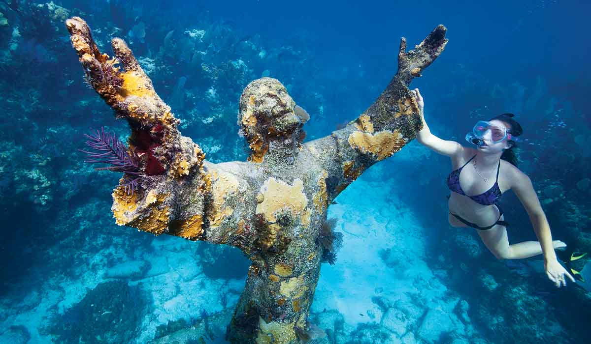 Bikini-clad snorkeler approaches a sunken Jesus statue