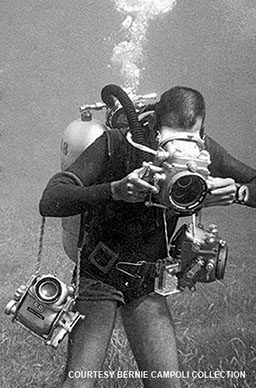 Black-and-white image of a diver holding three cameras