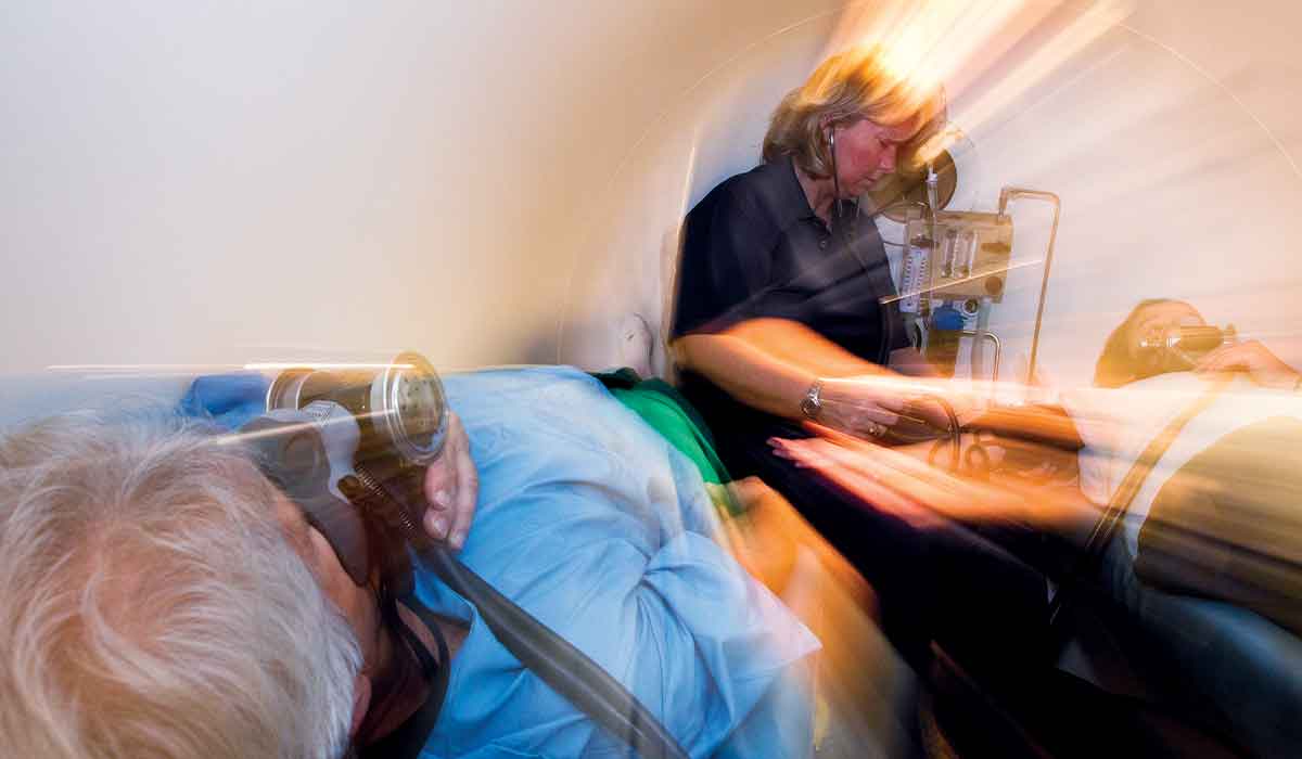 Blurry action photo of a nurse helping two patients inside a hyperbaric chamber