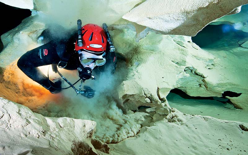 Cave diver in red helmet squeezes through a tight cave