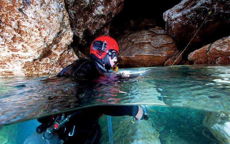 Cave diver in red helmet sticks head out of water
