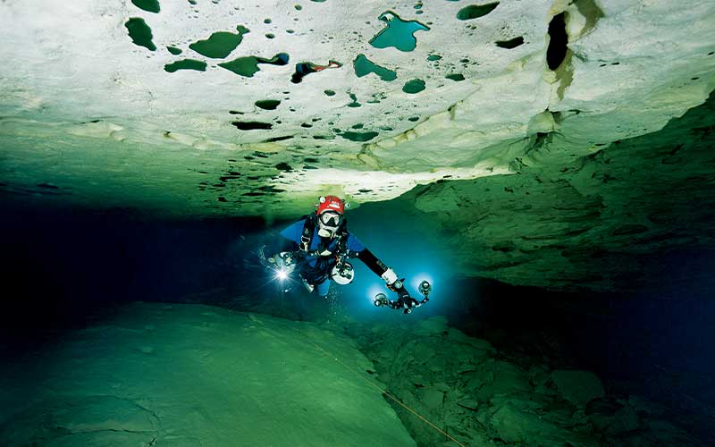 Cave diver swims through crevice holding two strobe lights