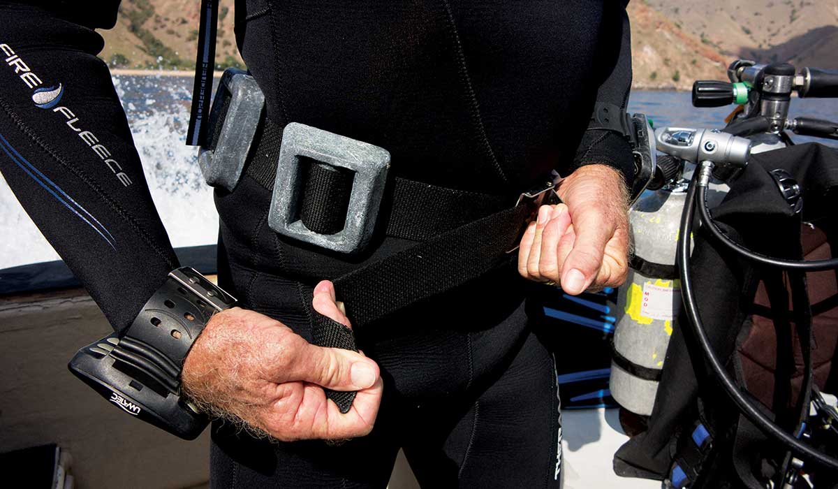 Close up of a diver's mid-section has he straps on his weight belt