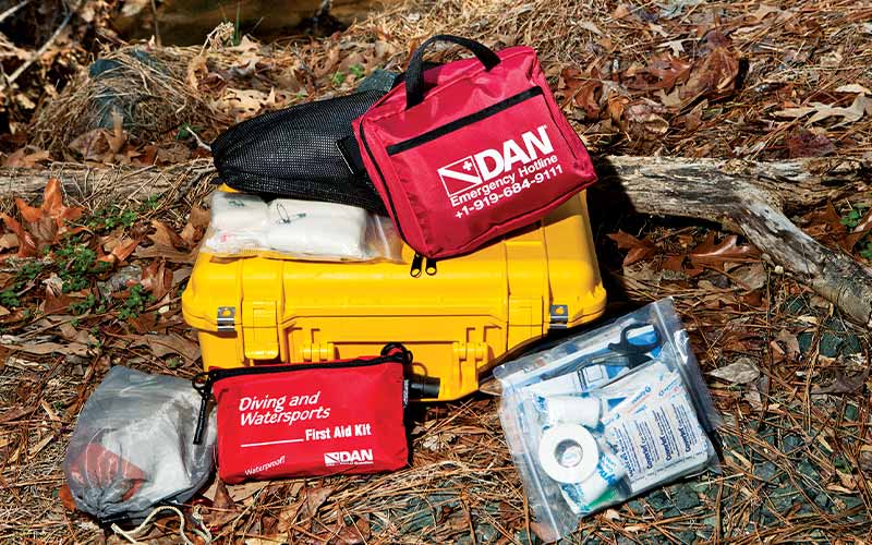 A hard-case DAN first aid kit is displayed on leafy ground
