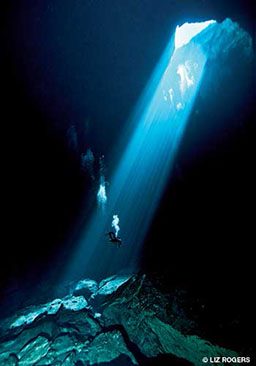 Diver can be seen in a stream of light from a cave